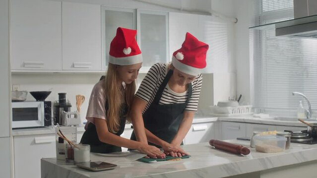 Wide shot of mom and daughter in Christmas hats making cookies at kitchen counter togetherWide shot of mom and daughter in Christmas hats making cookies at kitchen counter together
