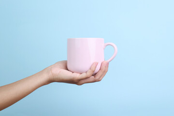 Hands Holding Pink Ceramic Mug Isolated on Blue Background