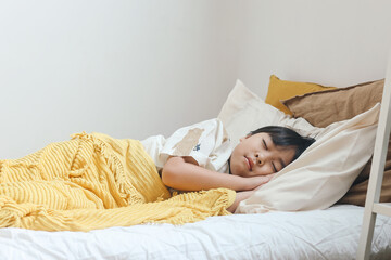 Asian boy wearing pajama sleeping on a bed in a bedroom.