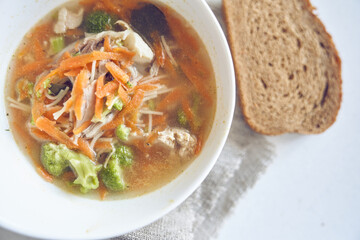 Top view of a healthy and delicious soup of vegetables and meat in a white plate on the table with bread with copy space. Bright soup with carrots, pieces of meat, broccoli. 