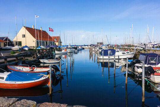 Dragør pier with multiple docked boats in water reflecting the blue sky and the Danish flag full mast