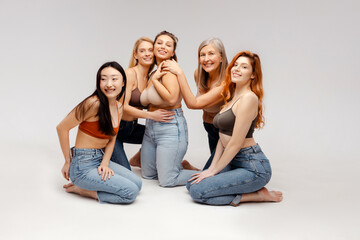 Group of diverse multiracial women wearing stylish bras and jeans sitting hugging looking at camera