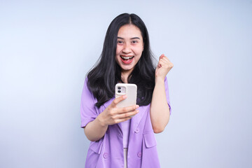 Excited Young Woman Looking at Good News on Smart Phone. Lucky Girl Gesture Winning Isolated on Gray Background