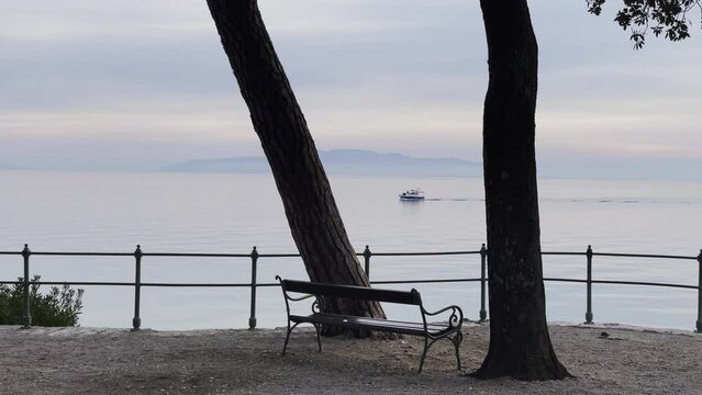 Boat passing by sea shore Resort town bench island in distance close up Lovran, Opatija, Croatia