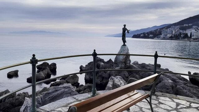Statue of a woman on sea shore bench Resort town island in distance Lovran, Opatija, Croatia