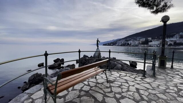 Statue of a woman on sea shore bench Resort town island in distance approached Lovran, Opatija, Croatia