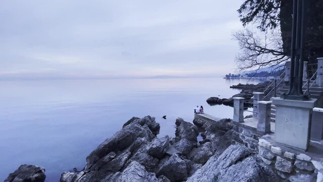 Couple sitting on Sea shore with island in distance fish eye wide Lovran, Opatija, Croatia