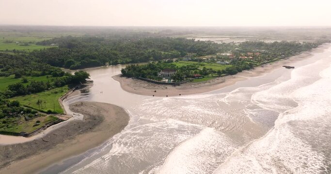 River mouth on coastline breaches into ocean with ATVs riding on beach, aerial