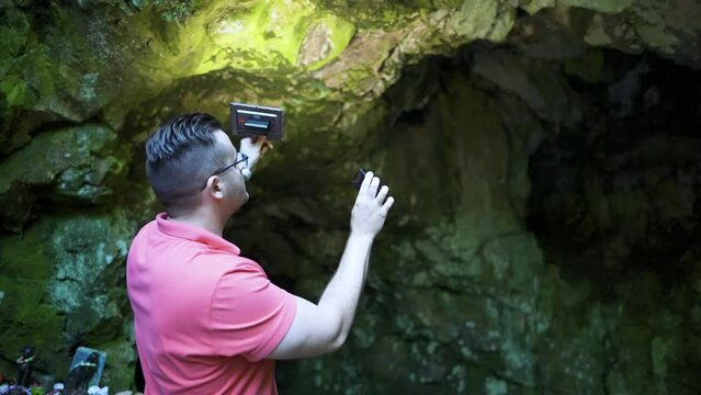 Holding up a recorder, a man is recording some environmental ambient sounds in front of a cave known as the location of the tomb of the Egyptian goddess Bastet at Strandzha Mountain in Bulgaria.
