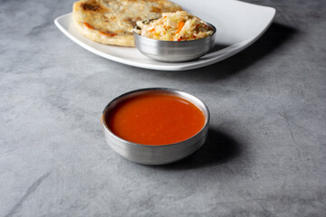 A view of a metal condiment cup of red salsa for pupusas.