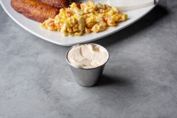 A view of a metal condiment cup of butter spread next to a plate of Salvadoran tipico.