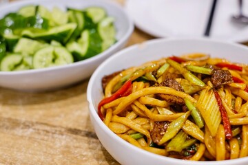 Goshilik lagman, a Uyghur dish of fresh handmade noodles stir-fried with meat and vegetables with a plate of garlic cucumber salad at Apandim Xinjiang Restaurant in Burwood Chinatown, Sydney, NSW
