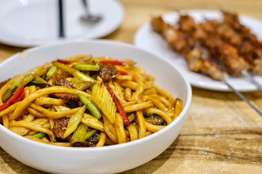 Goshilik lagman, a Uyghur dish of fresh handmade noodles stir-fried with meat and vegetables with a plate of grilled cumin lamb skewers at Apandim Xinjiang Restaurant in Burwood Chinatown, Sydney, NSW