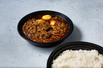 A view of a bowl of a Ayamase stew, with a container of white rice.