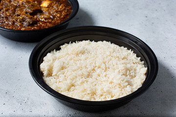 A view of a bowl of a container of white rice with Ayamase stew.