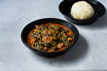 A top down view of a container of efo riro, with a ball of fufu.
