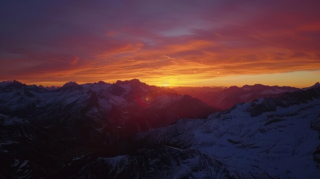 Majestic mountains silhouetted against a fiery sunset sky. The peaks are capped with snow,