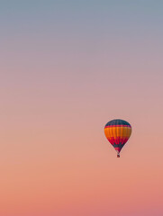 Fototapeta premium Dawn Ascension - A vivid hot air balloon rises in a tranquil dawn, its colors a stark contrast to the pastel hues of the early sky.