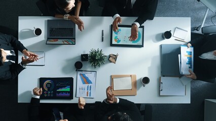 Top down aerial view of smart manager pointing at financial graph on whiteboard while diverse business team explain and plan marketing idea at meeting table with stock market statistic. Directorate.