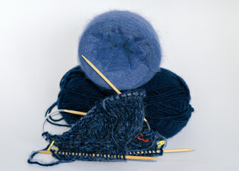 photo with knitting needles, balls of yarn and a piece of knitted jacket on a solid white background