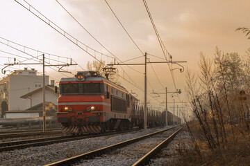 Freight train with red locomotive and some waggons is driving towards the camera in a mystical early morning setting ith sun about to rise.