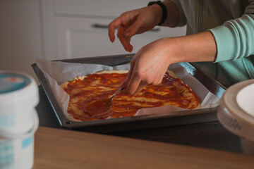 Woman is spreading home made tomato sauce on pizza dough spread in a pan. Home made pizza preparing to be baked at home