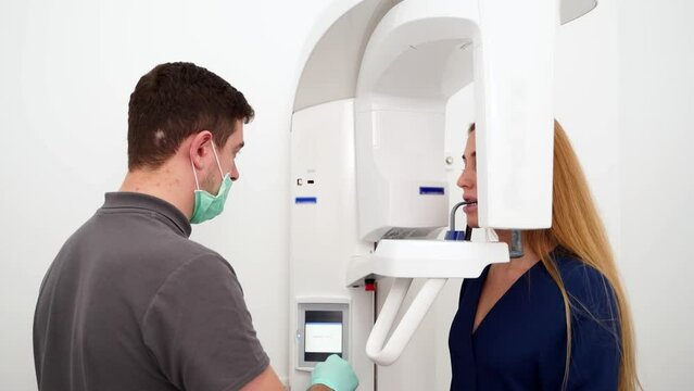 Male radiologist taking teeth x-ray of female patient using dental x-ray machine. Dentist adjusts scan projection by laser guide. Doctor doing digital x-ray tooth scan for woman in the dental clinic.