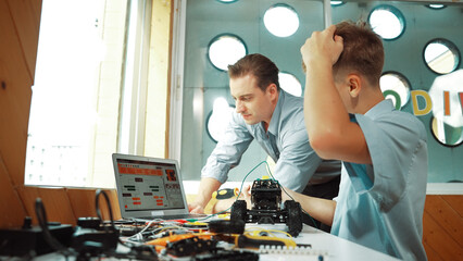 Caucasian teacher help student fixing car model and giving advise for programing system or coding...