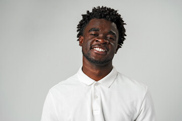 Fototapeta premium Young African Man With a Joyful Smile in White Shirt Against Gray Background