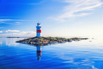 Lighthouse on a rocky islet with reflections in the water a sunny summer day