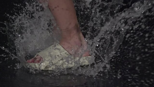 A joyful person splashes in water puddle with sandals, creating energy