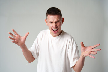 Angry young man screaming on gray background in studio
