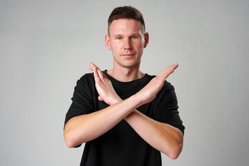 Young man showing x sign with crossed hands, meaning stop on gray background