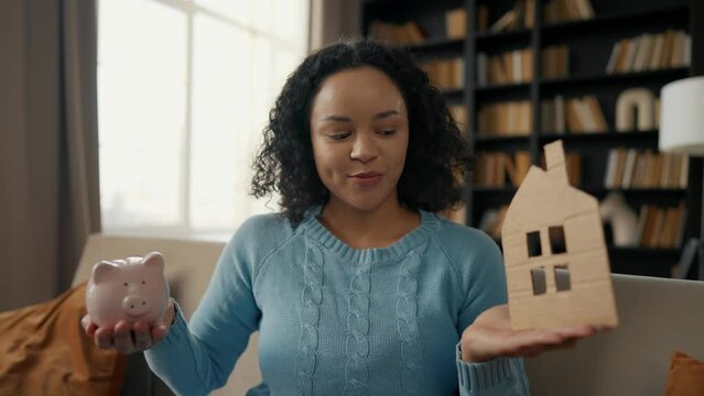 Young girl is saving money for a house. African american female teenager holding cardboard shape of house, dream of housing relocation renting new flat. Child dreaming of future, saving money concept.