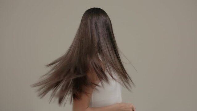 A brunette girl with long straight hair poses in the studio against a light background.