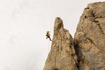A man is climbing a rock face with a green rope. Concept of adventure and excitement, as the man is...