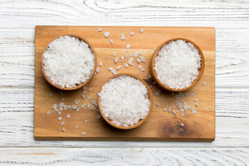 A wooden bowl of salt crystals on a wooden background. Salt in rustic bowls, top view with copy space