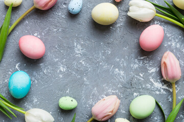 Happy Easter composition. Easter eggs on colored table with yellow Tulips. Natural dyed colorful eggs background top view with copy space