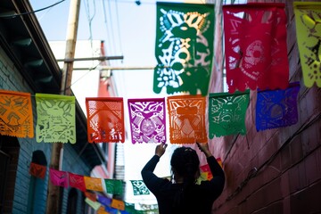 person hanging colorful papel picado banners across alley