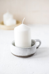 A thick candle in a ceramic candlestick on the background of three burning candles.