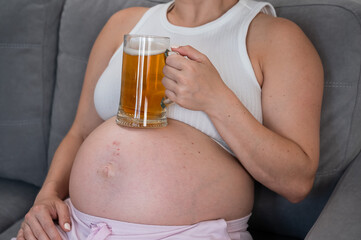 A faceless pregnant woman sits on the sofa and holds a glass of beer on her stomach. Skin rash. 