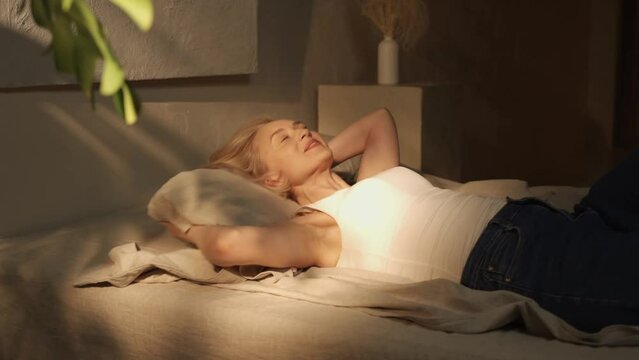 In the warmth of a soft-loft bedroom, an woman joyfully collapses onto a plush bed, sinking into the comfort of the inviting bedding. The ambiance exudes calmness and relaxation 