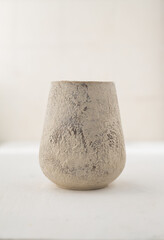 A light handmade clay vase with a rough texture on a white table. light colors. Front view....