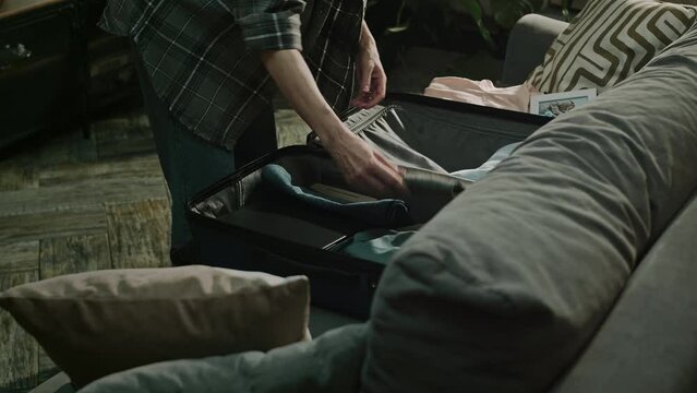 Lowkey handheld shot of Caucasian mature battered woman packing her clothes in suitcase fast while preparing to leave toxic and abusive relationship with husband and not go back