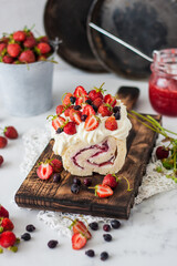 meringue roll with cream and summer homemade berries. The roll is entirely on a wooden board on a light background. Close-up. Rustic style, homely and cozy.