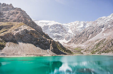 Blue turquoise lake Kulikalon against the backdrop of rocky mountains with glaciers on a warm sunny morning in the Fan Mountains in Tajikistan, landscape in the mountains