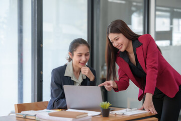 Two women are sitting at a desk looking at a laptop