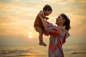 happy mother holding and lifting with toddler baby girl on the sea beach at sunset