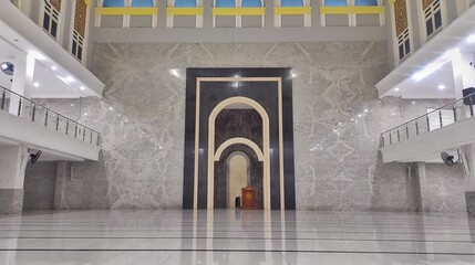 The empty praying hall of mosque with white marby tiled floor and wall