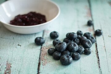 Blueberry pile next to blueberry jam in white bowl.